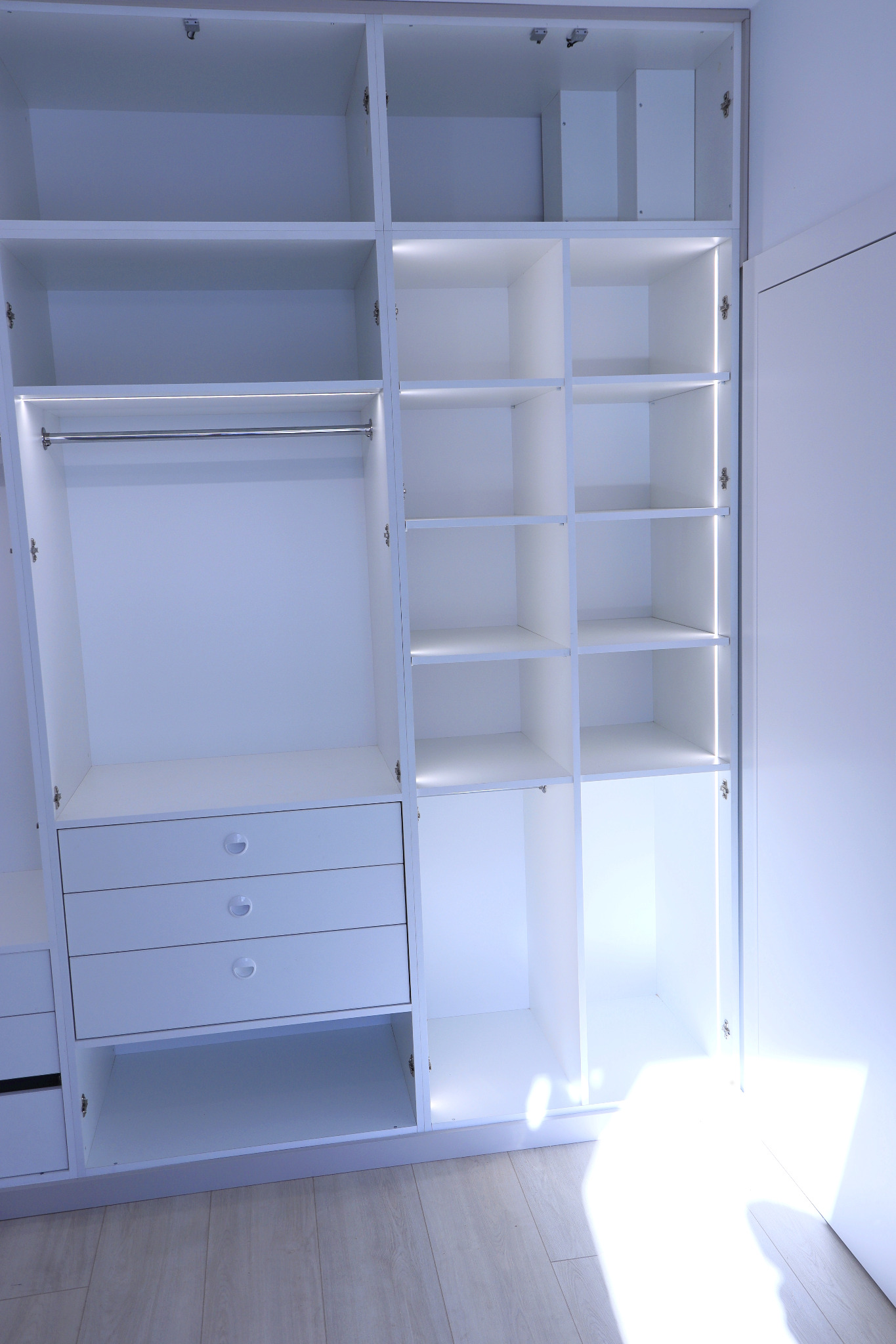 Wnętrze białej szafy na wymiar z oświetleniem LED, widoczne półki, drążek na ubrania oraz szuflady z okrągłymi uchwytami.