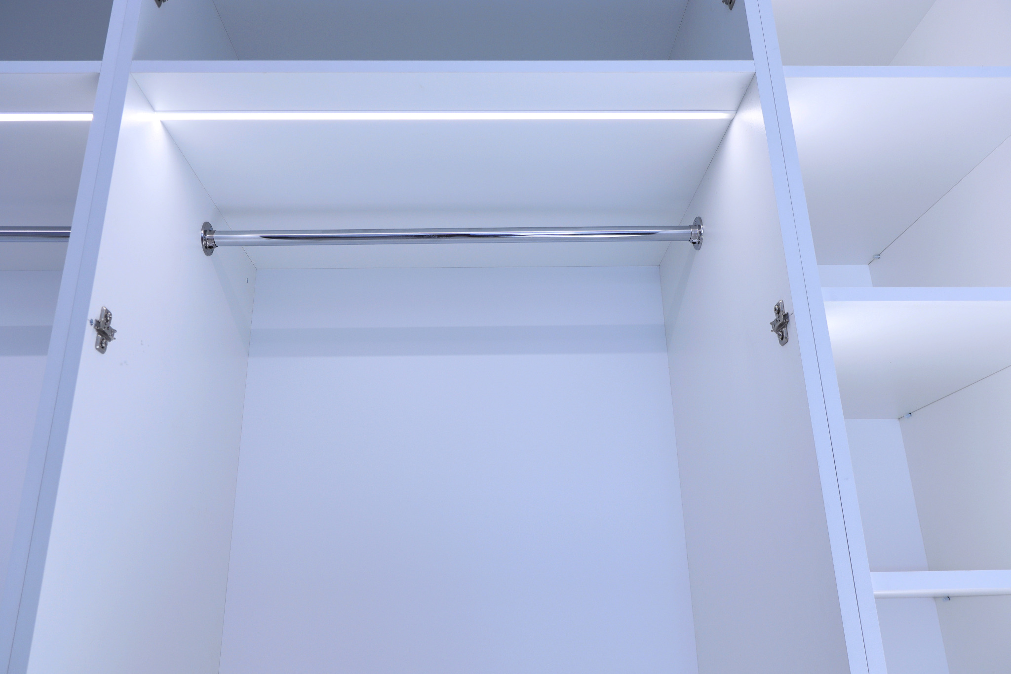 Wnętrze białej szafy z drążkiem na ubrania i oświetleniem LED w Lublinie, widok od dołu.