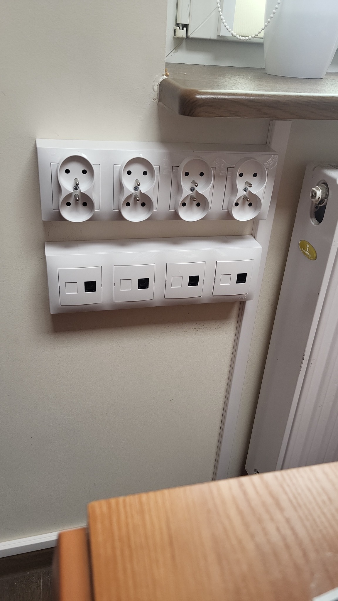 Cztery podwójne gniazdka elektryczne Schuko i cztery gniazda sieciowe RJ45 zamontowane w rzędzie na ścianie, widoczne ślady montażu.