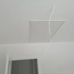 Biały sufit z kwadratową klapą rewizyjną, z której zwisa kabel elektryczny, widoczny fragment białej ściany i futryna drzwi.