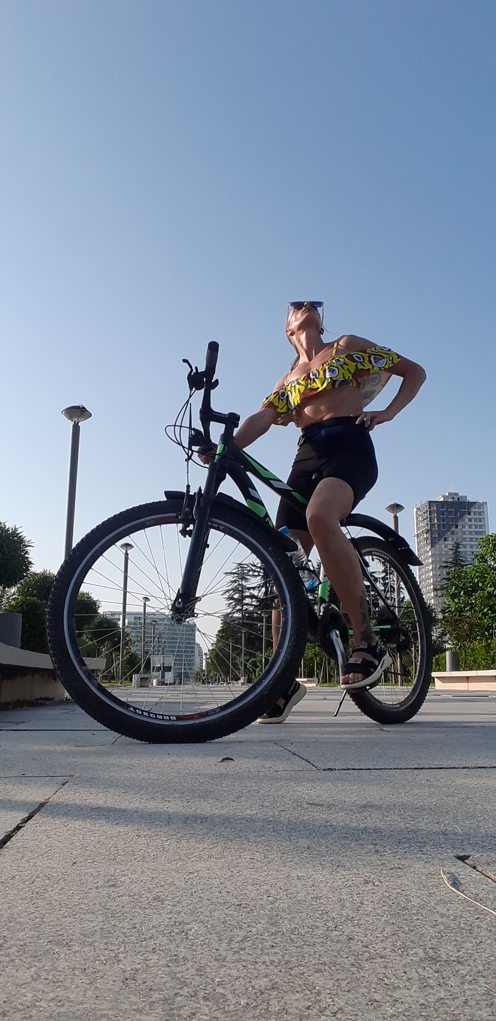 Kobieta w sportowym stroju pozuje na rowerze górskim na tle miejskiego krajobrazu z budynkami i latarniami