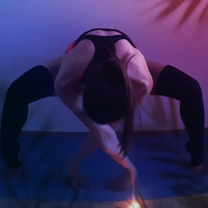 Kobieta w pozie mostu na macie do ćwiczeń, ubrana w czarne podkolanówki i strój do ćwiczeń, oświetlona niebiesko-różowym światłem