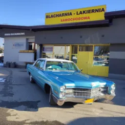 Błękitny, odrestaurowany Cadillac z białym dachem zaparkowany przed budynkiem warsztatu z żółtym szyldem. W tle widoczne biuro rachunkowe i resztki śniegu.