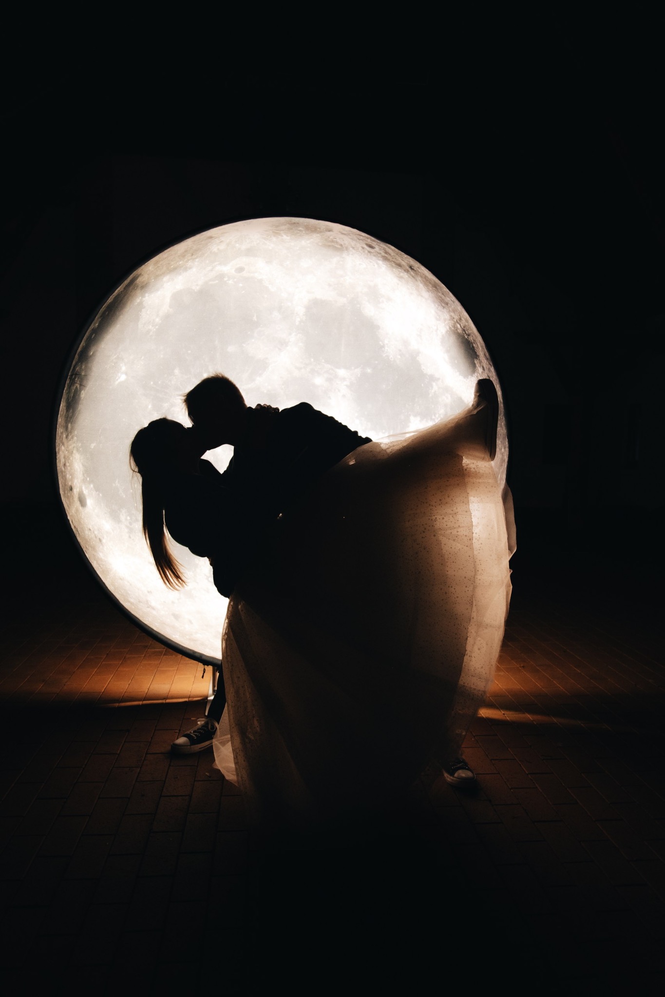 Sylwetki całującej się pary na tle księżyca. Panna młoda w sukni i trampkach. Nastrojowe oświetlenie. Romantyczna sesja w plenerze.