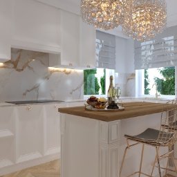 DomiDesign Projektowanie wnętrz - Elegancka, biała kuchnia z marmurowym blatem i złotymi akcentami, wyspa z drewnianym blatem, kryształowy żyrandol, dekoracyjne słoiczki na blacie