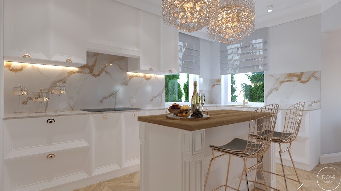 Elegancka, biała kuchnia z marmurowym blatem i złotymi akcentami, wyspa z drewnianym blatem, kryształowy żyrandol, dekoracyjne słoiczki na blacie