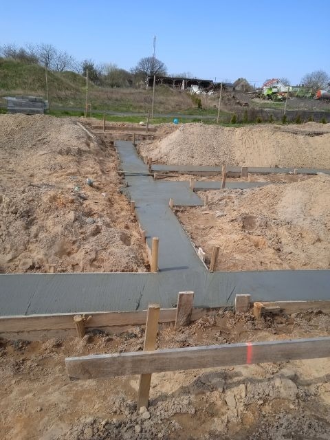 Wylany beton w szalunku fundamentów na placu budowy w słoneczny dzień, widok z góry na przygotowany zarys budynku.