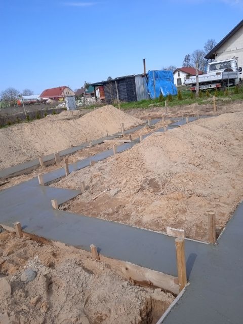 Wylany beton w szalunkach pod fundament domu jednorodzinnego w Świdwinie, widoczne drewniane stemple i pryzmy piasku.