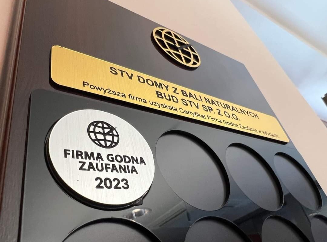 Tablica z certyfikatami firmy STV Domy z Bali Naturalnych, zawierająca złoty napis i srebrny medalion 'Firma Godna Zaufania 2023', umieszczona na ciemnym tle.