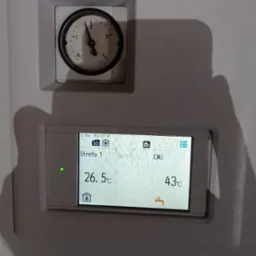 Panel sterowania z wyświetlaczem temperatury strefy 1 (26.5°C) i ciepłej wody użytkowej (43°C) oraz manometrem wskazującym ciśnienie w instalacji.