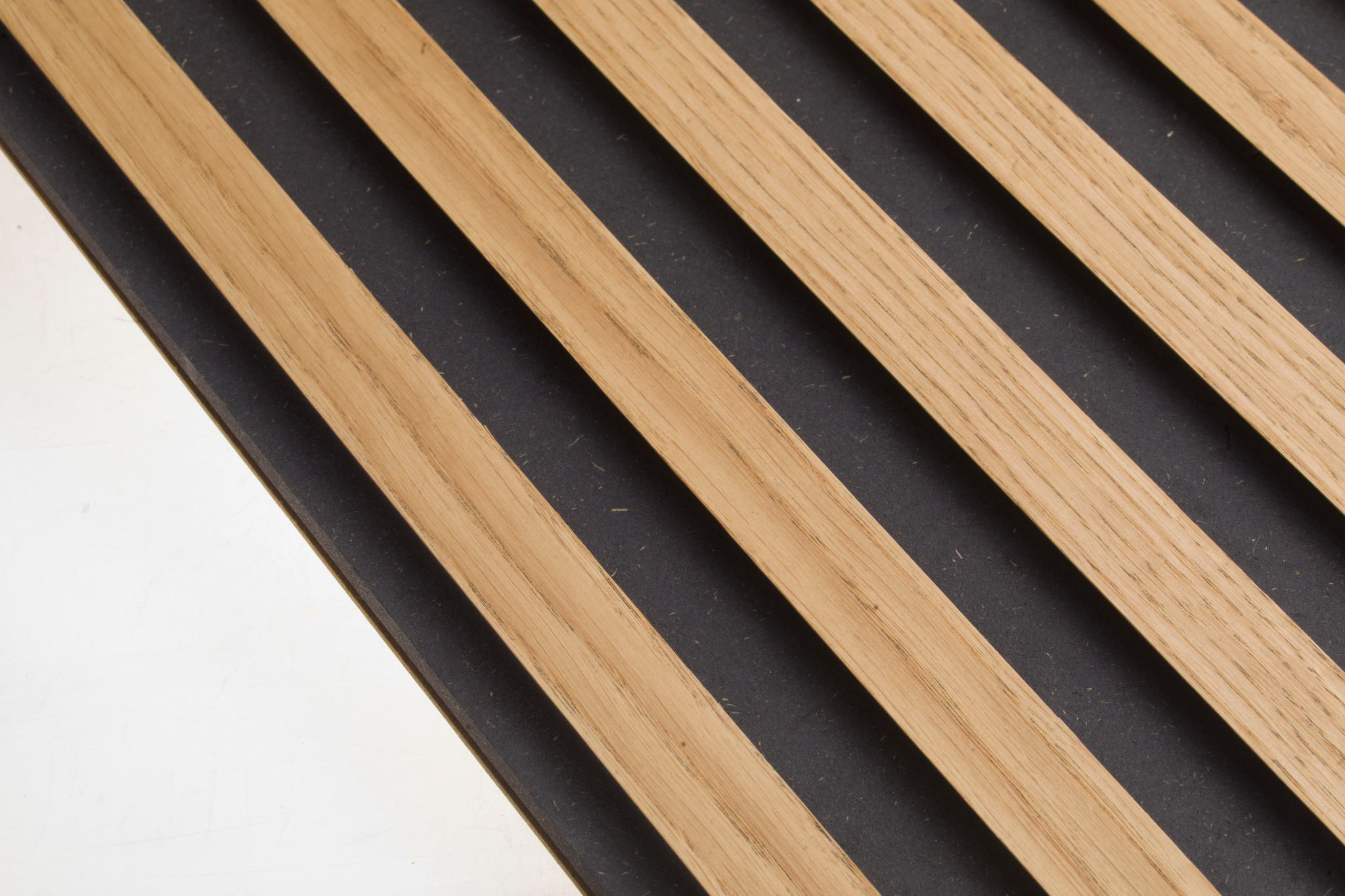 Dekoracyjne panele ścienne z naturalnego forniru dębowego, przymocowane do czarnej płyty HDF z filcowym podkładem, ułożone ukośnie na białym tle.