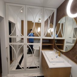 HOHO PROJEKT Adam Śleszyński - Nowoczesna łazienka z szafą wnękową z lustrzanymi drzwiami z dekoracyjnymi wycięciami, umywalką na drewnianej szafce i okrągłym lustrem z podświetleniem LED, widoczne czarno-białe płytki podłogowe.