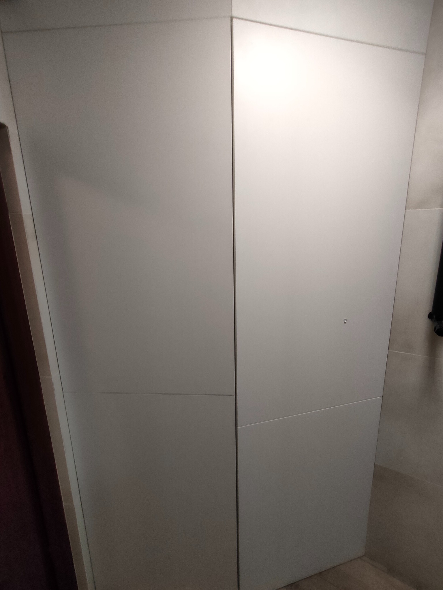 Minimalistyczna, biała szafa wnękowa z ukrytymi zawiasami, wkomponowana w jasne wnętrze. Proste linie i brak uchwytów podkreślają nowoczesny design.