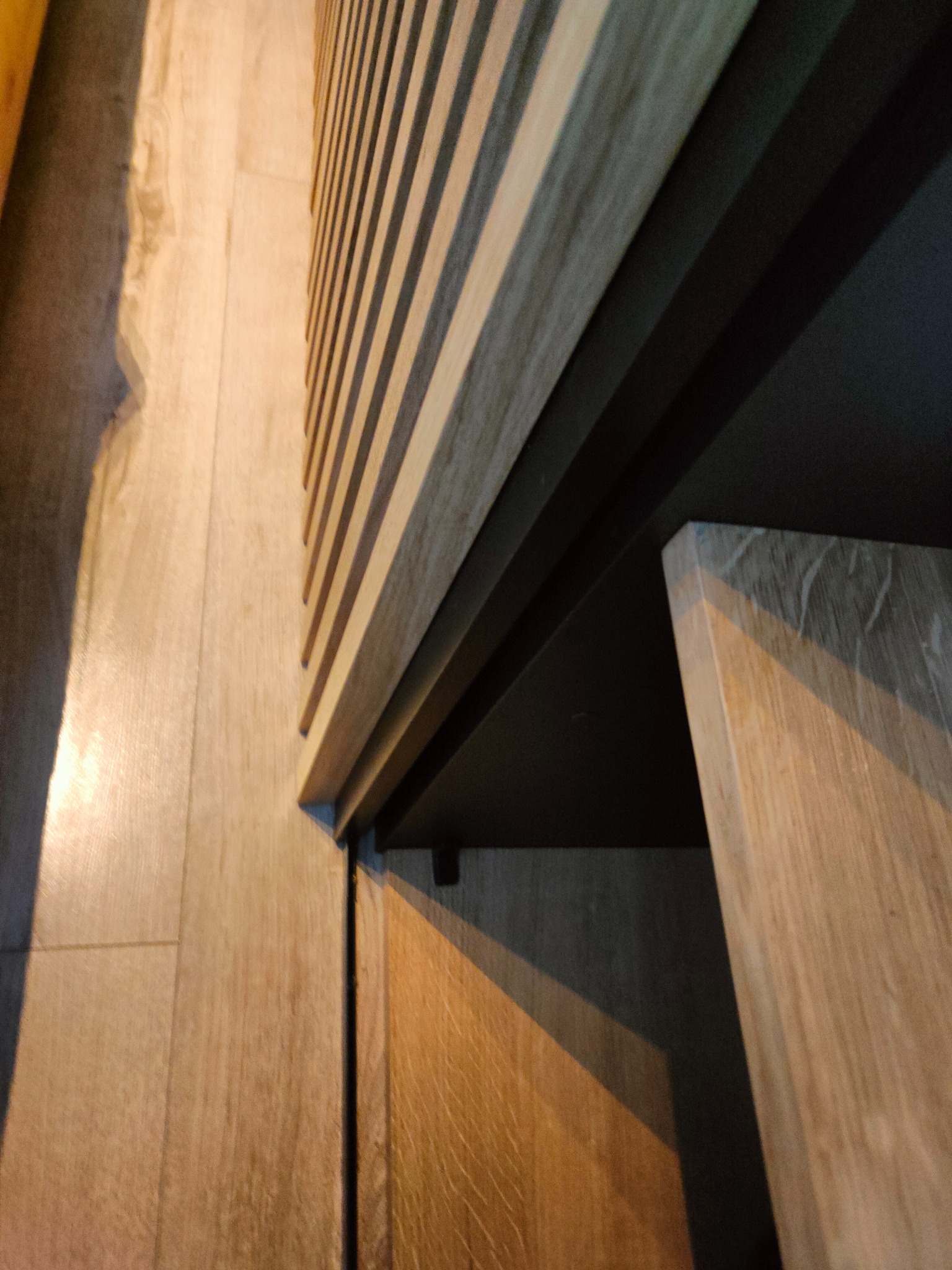 Nowoczesna szafa z lamelami i drewnianymi frontami, widok z dołu, ukazujący detale konstrukcyjne i materiały. Minimalistyczny design i precyzja wykonania.