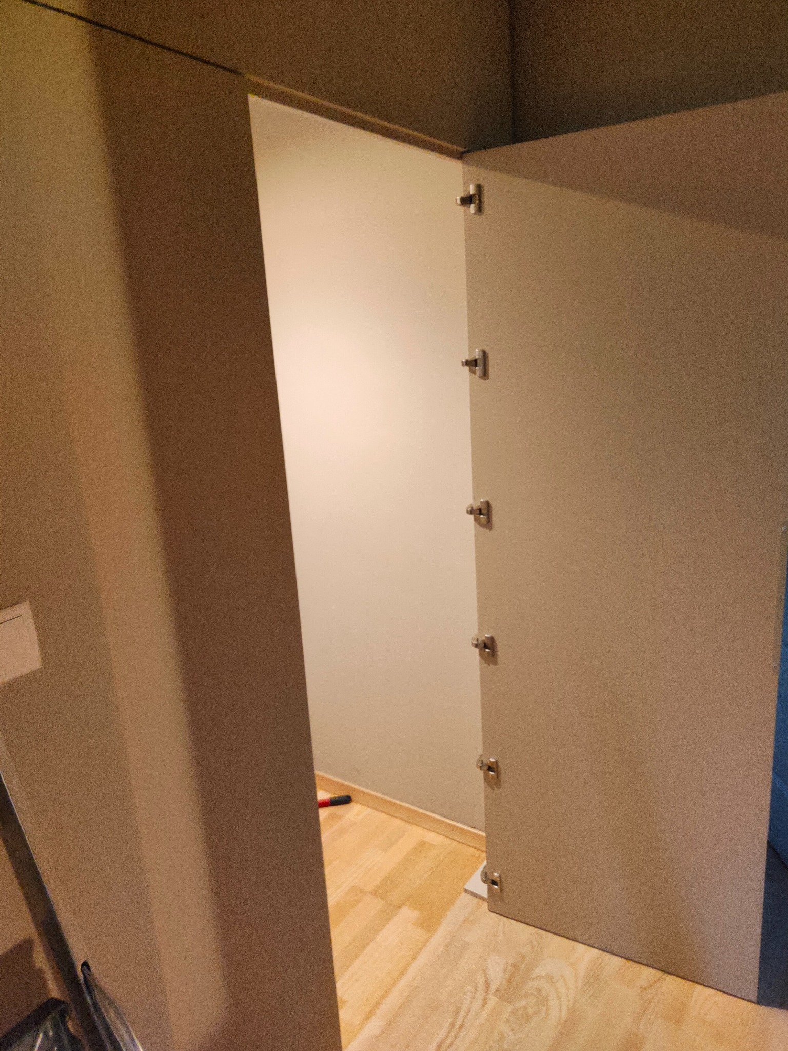 Otwarta szafa wnękowa z widocznymi zawiasami i wnętrzem. Ujęcie z bliska, ukazujące detale montażu i wykończenia. Podłoga z paneli.