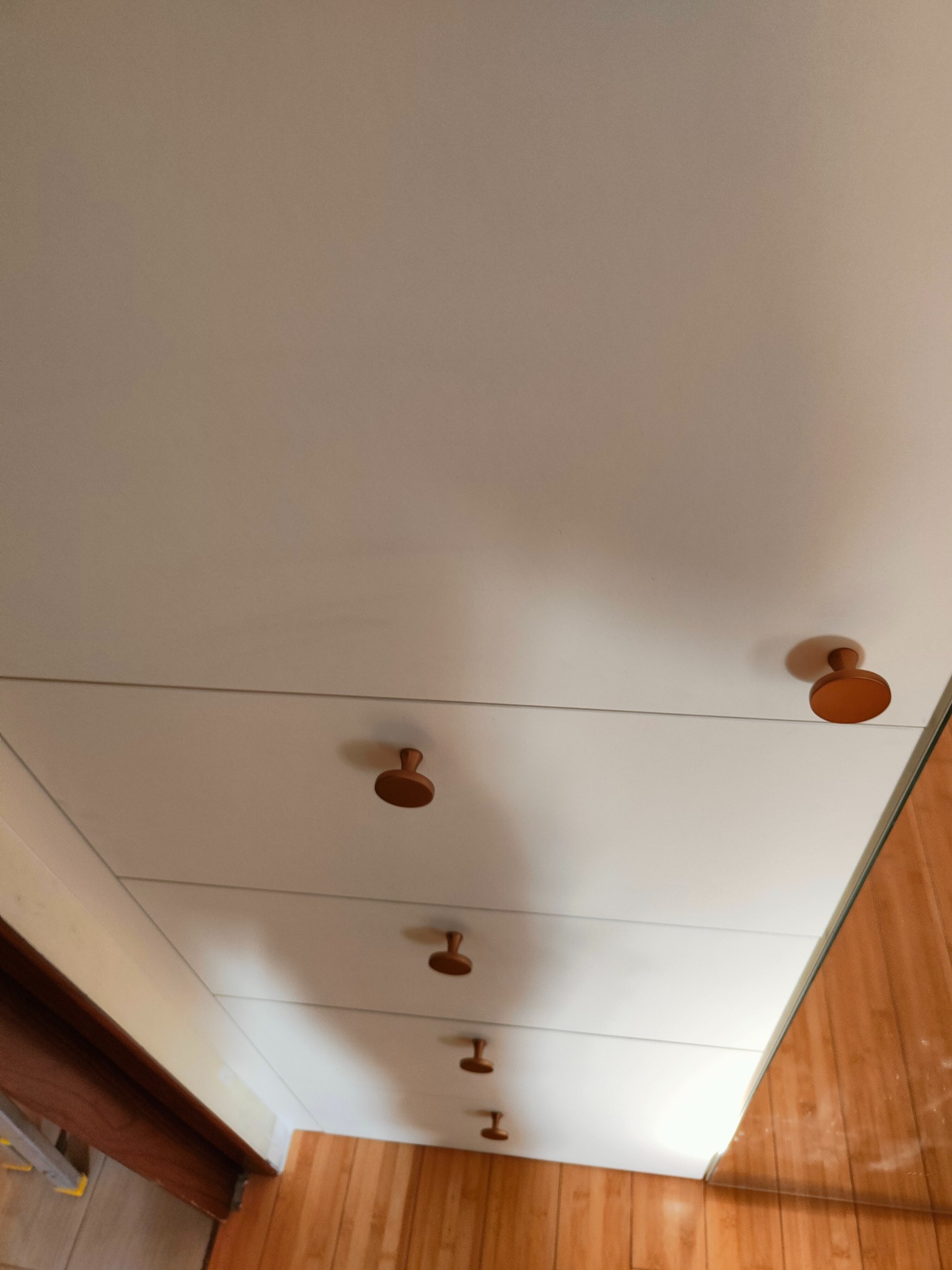 Biała szafa z drewnianymi uchwytami w mieszkaniu w Warszawie. Ujęcie z dołu, widoczne drewniane panele podłogowe i fragment drabiny.