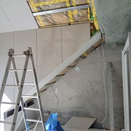 Ryszard Biłyk - Montaż płyt karton-gips na poddaszu. Widoczna izolacja, stelaż, płyty oraz drabina. Prace wykończeniowe w surowym wnętrzu.