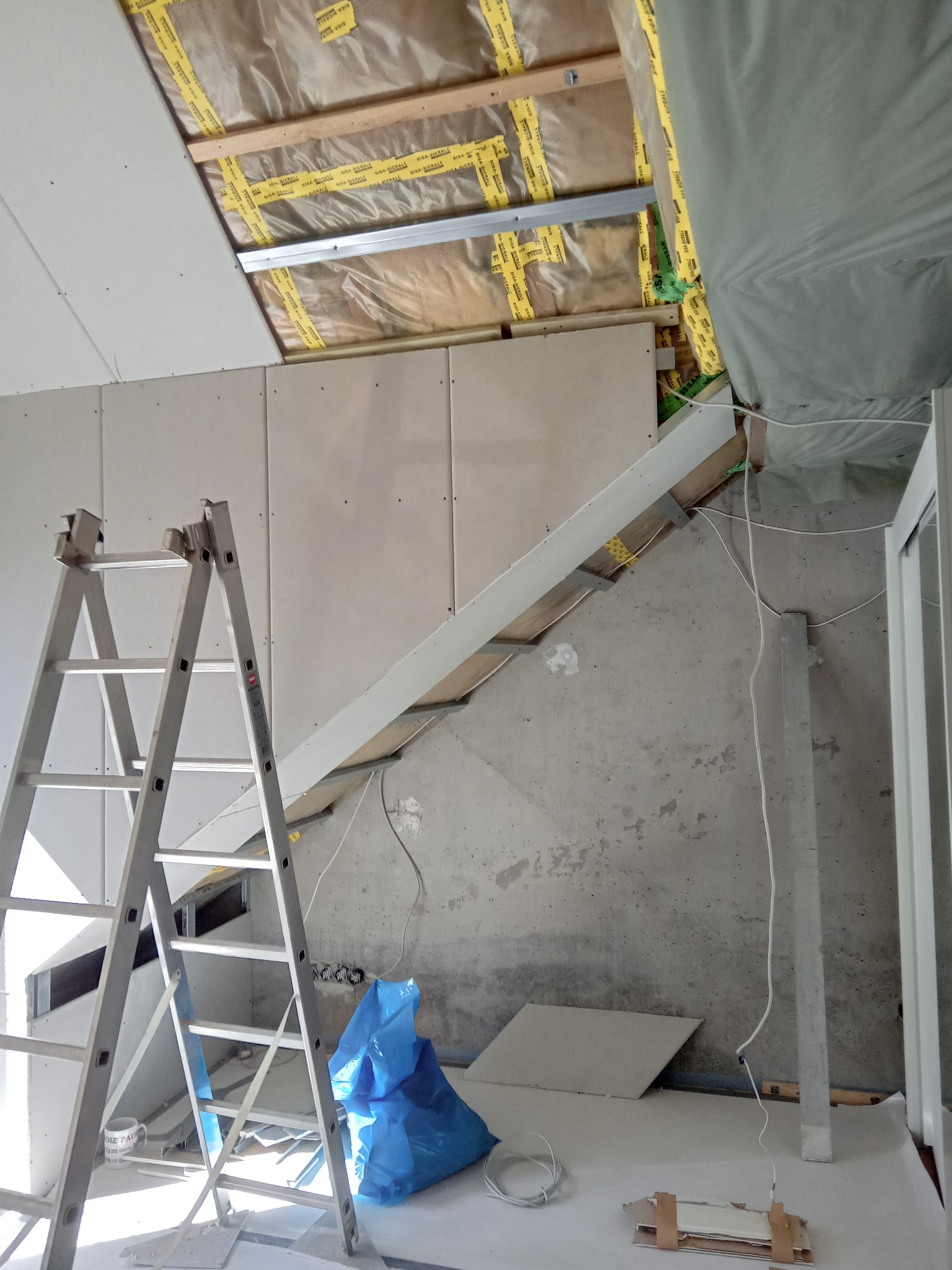 Montaż płyt karton-gips na poddaszu. Widoczna izolacja, stelaż, płyty oraz drabina. Prace wykończeniowe w surowym wnętrzu.