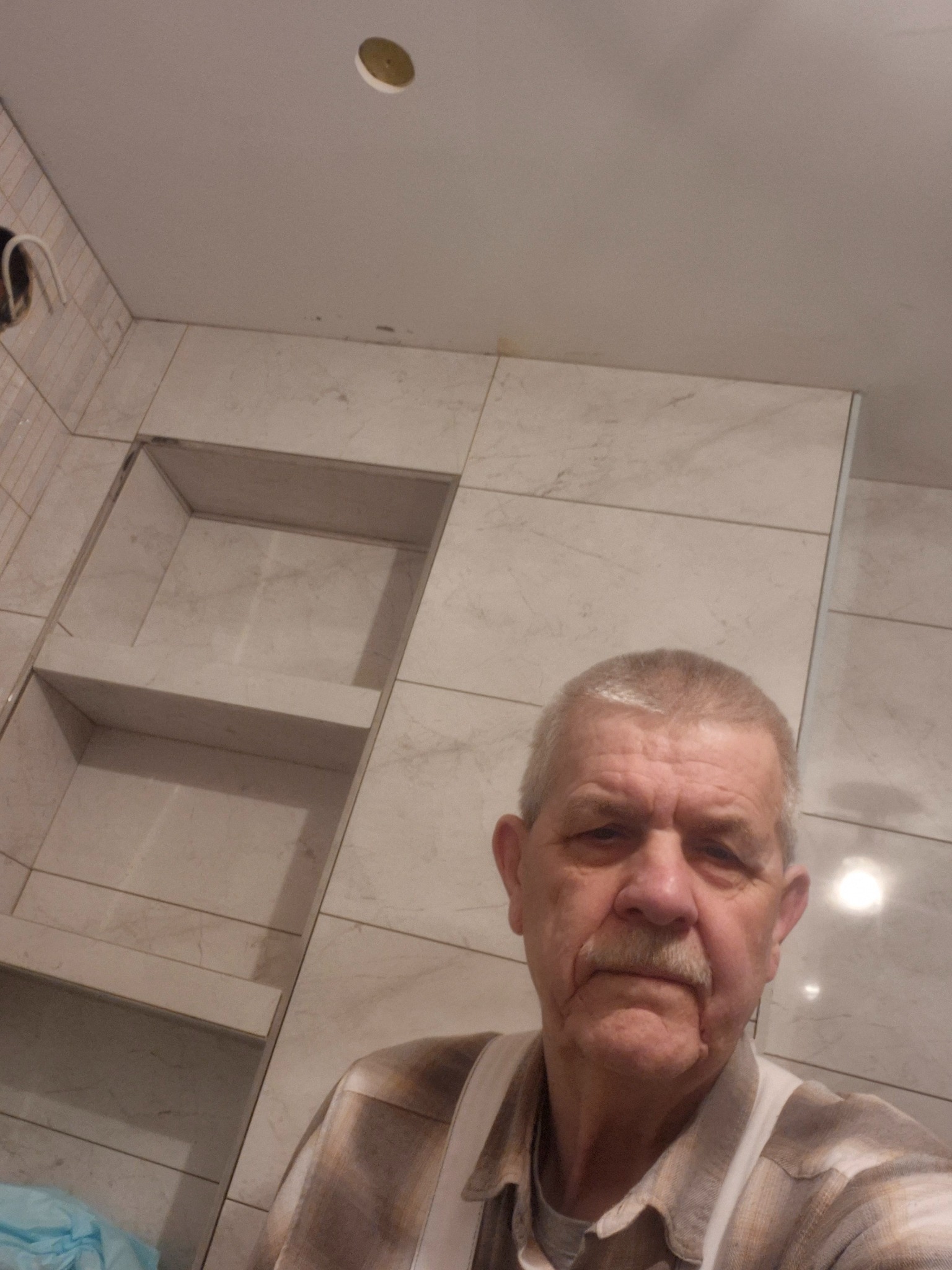 Wykończona ściana w łazience z wnękami wyłożona płytkami imitującymi marmur, widoczna osoba w tle. Nietypowy kadr z bliska.