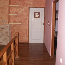 Korytarz po remoncie z drewnianą podłogą, ścianą w odcieniach pomarańczy z półkami i białą wewnętrzną stolarką drzwiową z naklejoną grafiką dłoni.