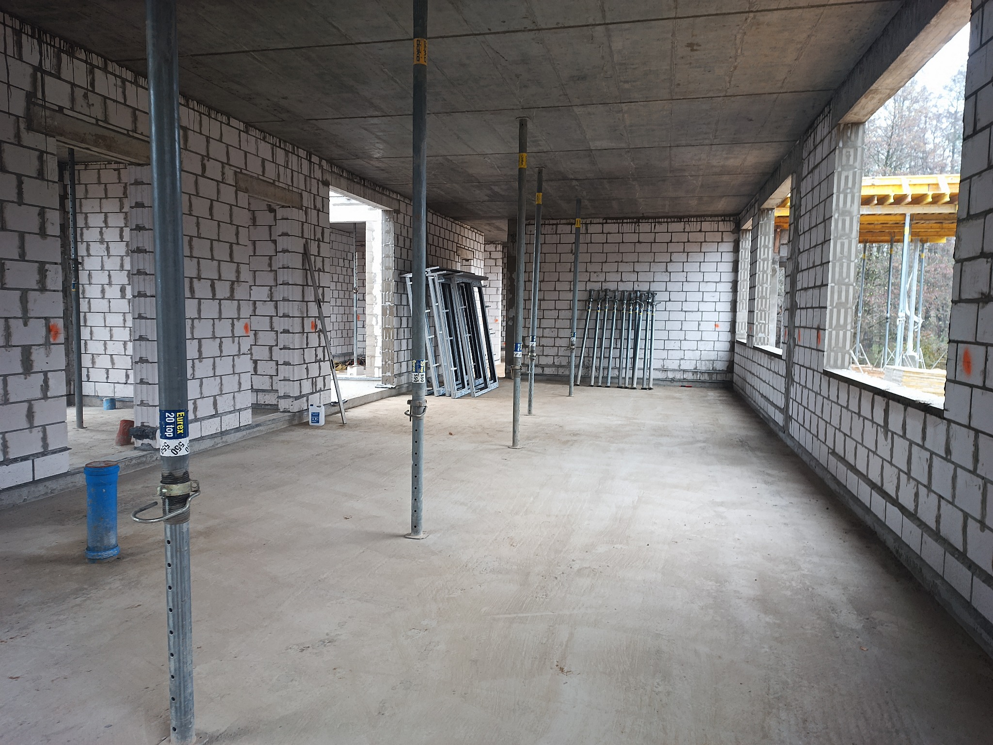 Wnętrze surowego domu w trakcie budowy z białych bloczków, widoczne stalowe podpory stropu, szalunki okienne i drzwiowe.