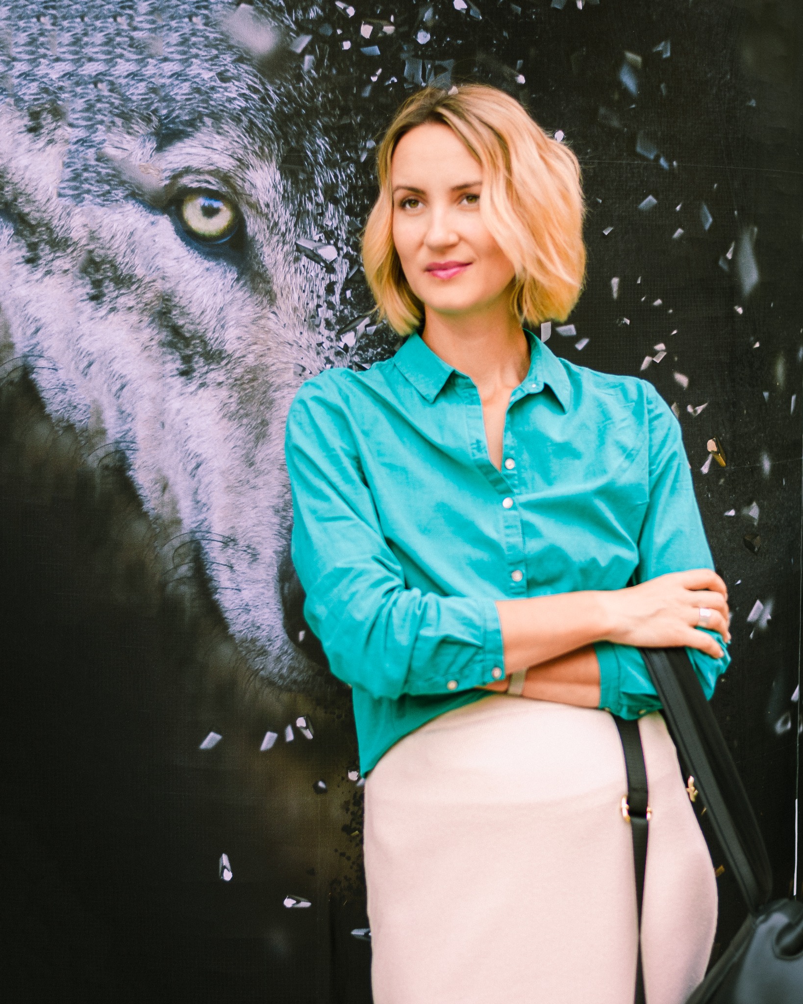 Kobieta w turkusowej koszuli pozuje na tle plakatu z wilkiem i efektem rozbicia szkła.