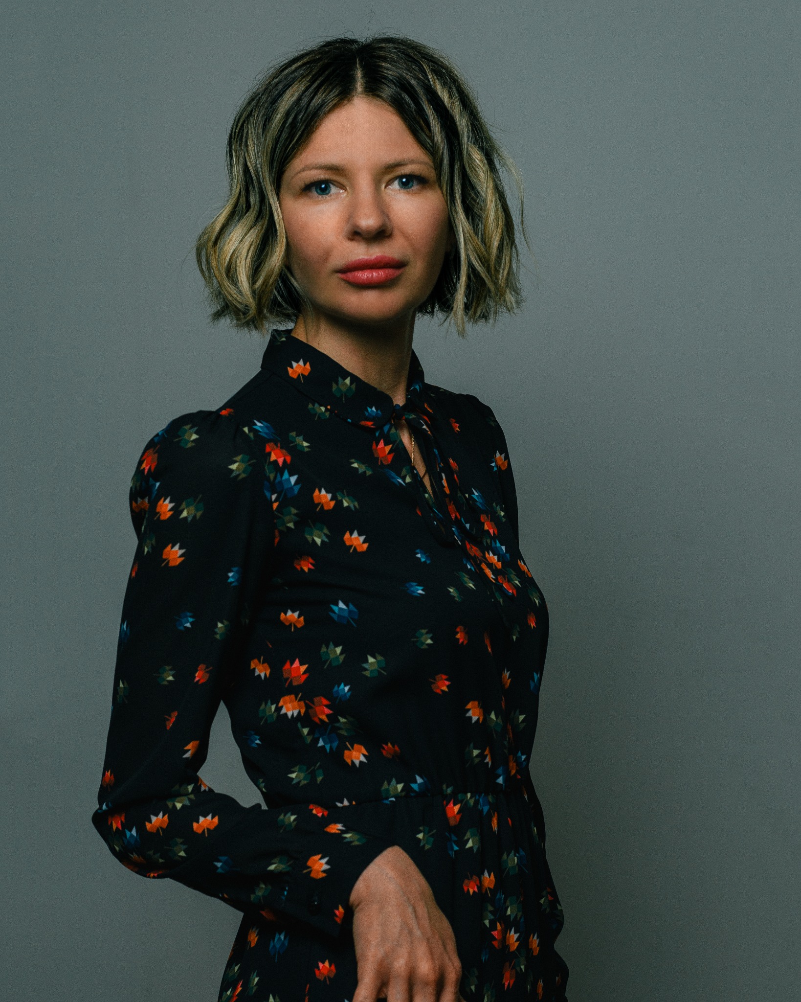 Portret kobiety z blond włosami w czarnej sukience w kolorowe liście na szarym tle.