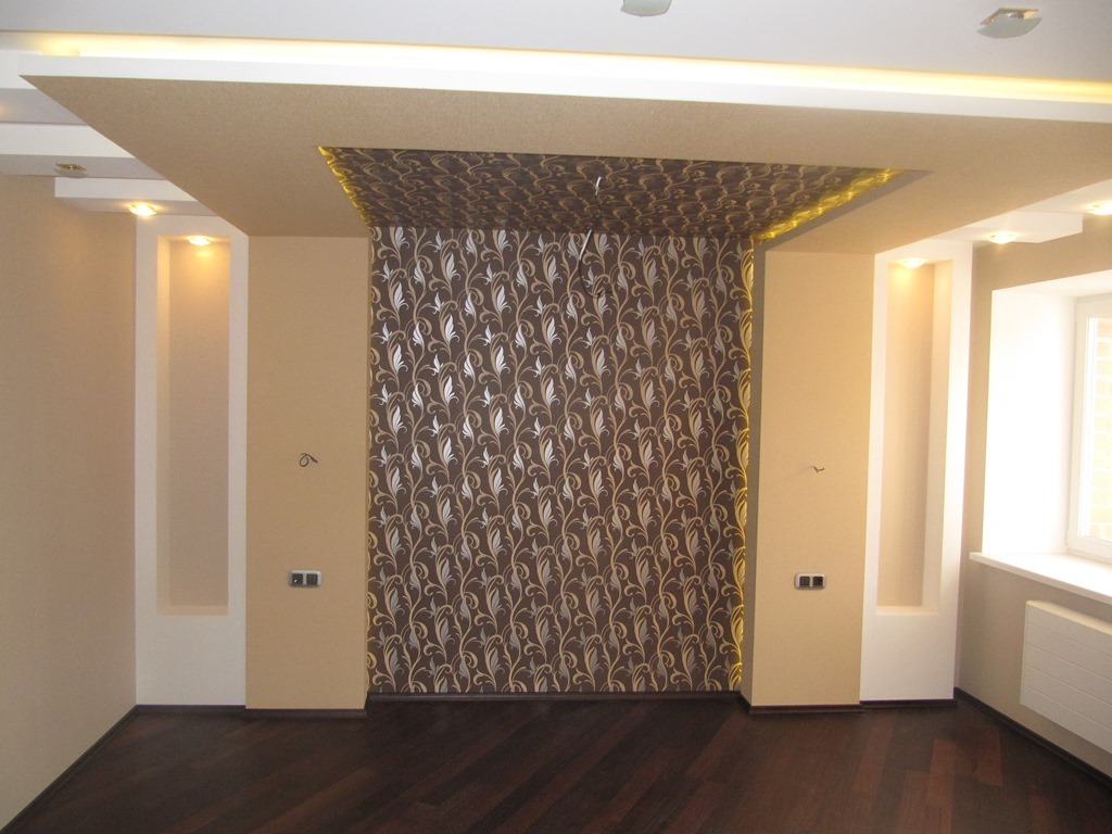 Ściana akcentowa z tapetą w brązowo-srebrne ornamenty roślinne, podwieszany sufit z oświetleniem LED, wnęki ścienne z podświetleniem, ciemna podłoga, widok na fragment okna z grzejnikiem.