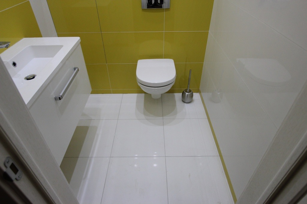 Nowoczesna łazienka z żółtymi i białymi płytkami, białą umywalką z szafką i toaletą, widok z perspektywy wejścia.