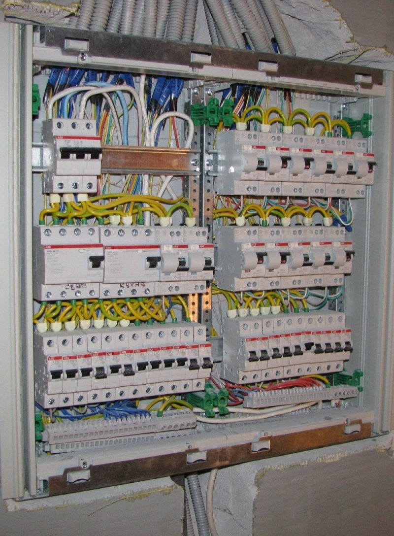 Otwarta skrzynka elektryczna z bezpiecznikami i okablowaniem w trakcie montażu; widoczne przewody w różnych kolorach oraz listwy zaciskowe.