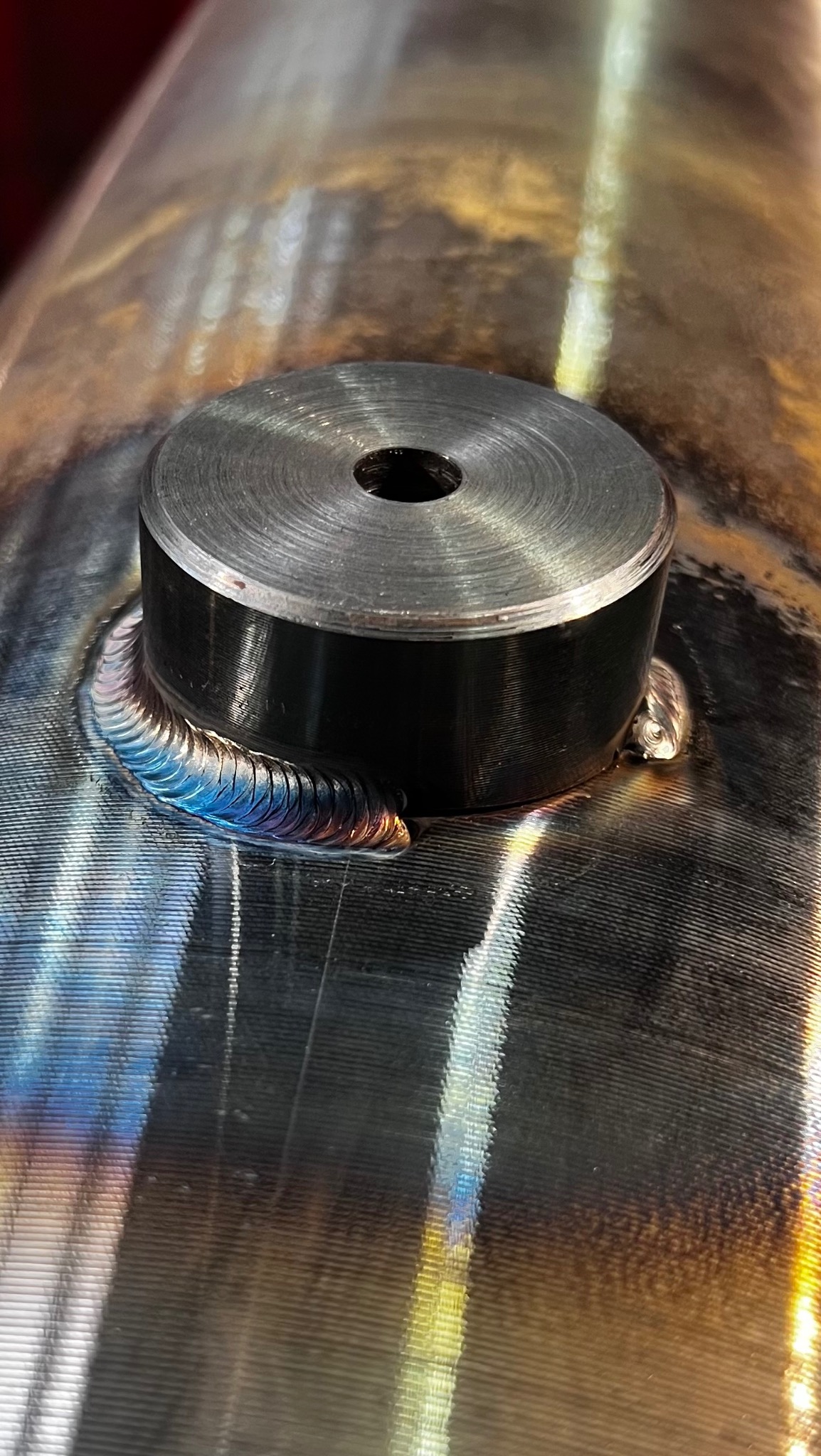 Metalowa rura z przyspawanym elementem, widoczne ślady po spawaniu z charakterystycznymi kolorami.