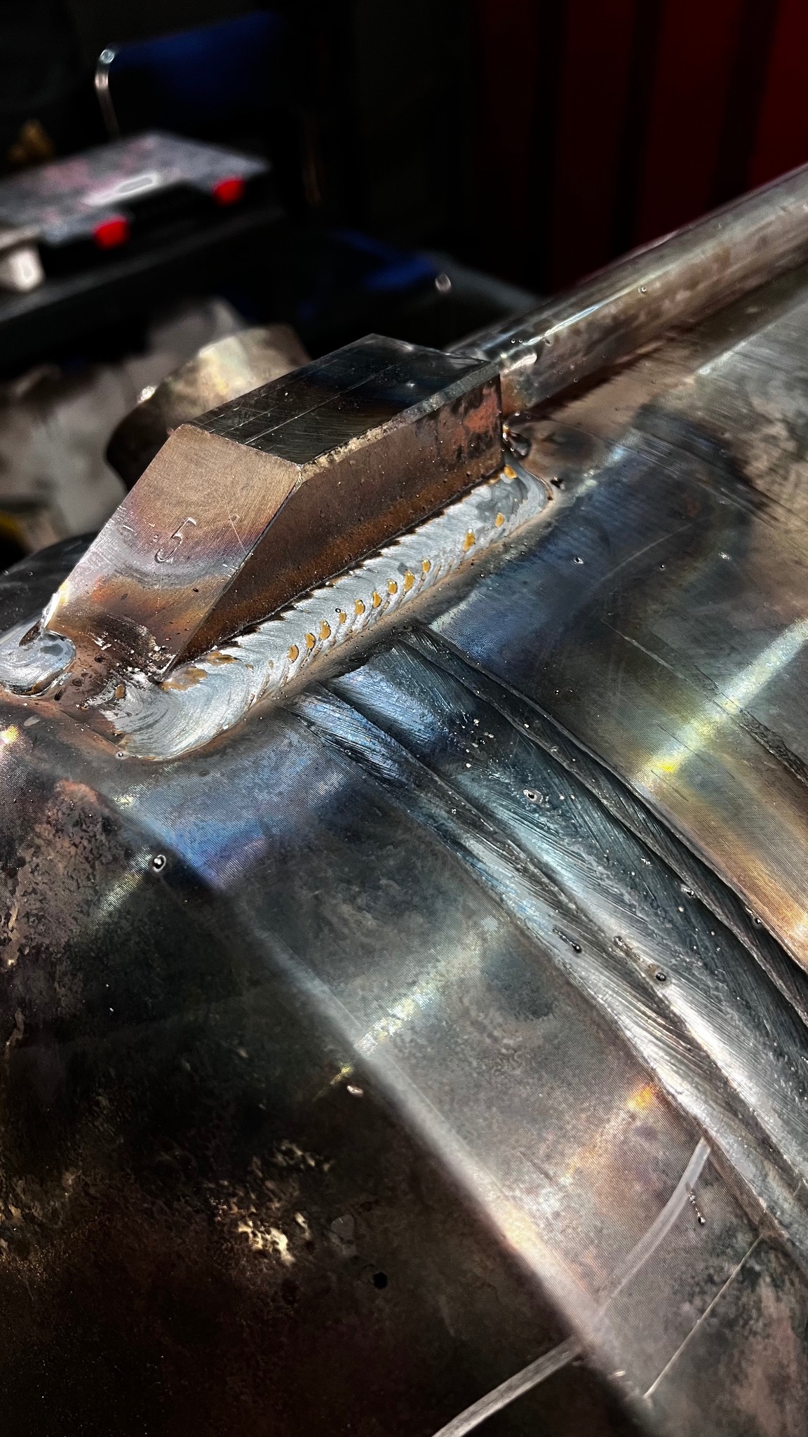 Spoina na metalowej rurze, wykonana metodą punktową, widoczne ślady obróbki i niewielkie krople na powierzchni.