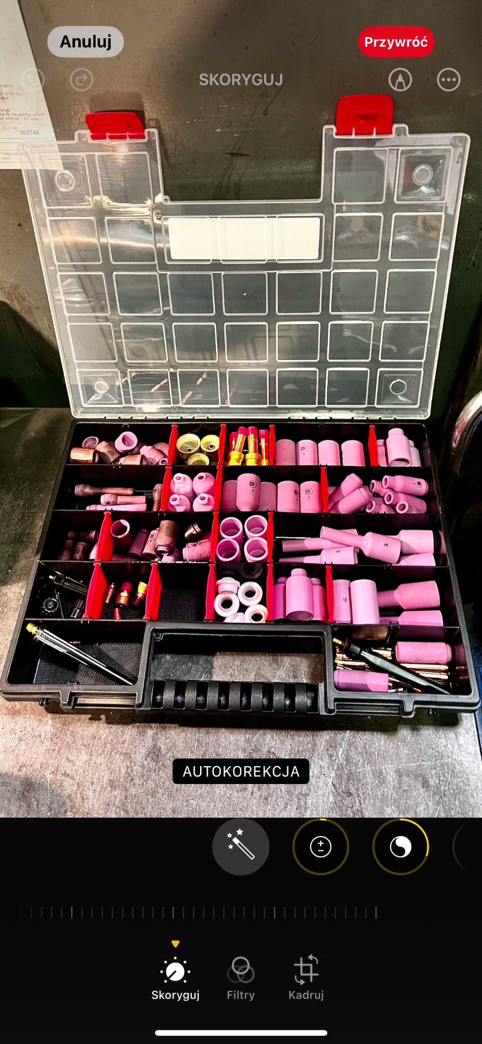 Otwarty organizer z przezroczystą pokrywą, wypełniony różnorodnymi dyszami i elektrodami spawalniczymi w odcieniach różu, czerwieni i mosiądzu, uporządkowanymi w przegródkach z czerwonymi...