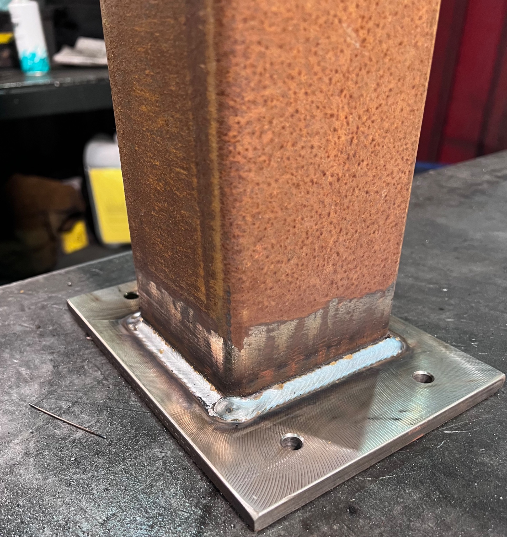 Zespawany, rdzawy profil kwadratowy z grubą, gładką płytą stalową, widoczne spoiny i ślady obróbki na płycie.