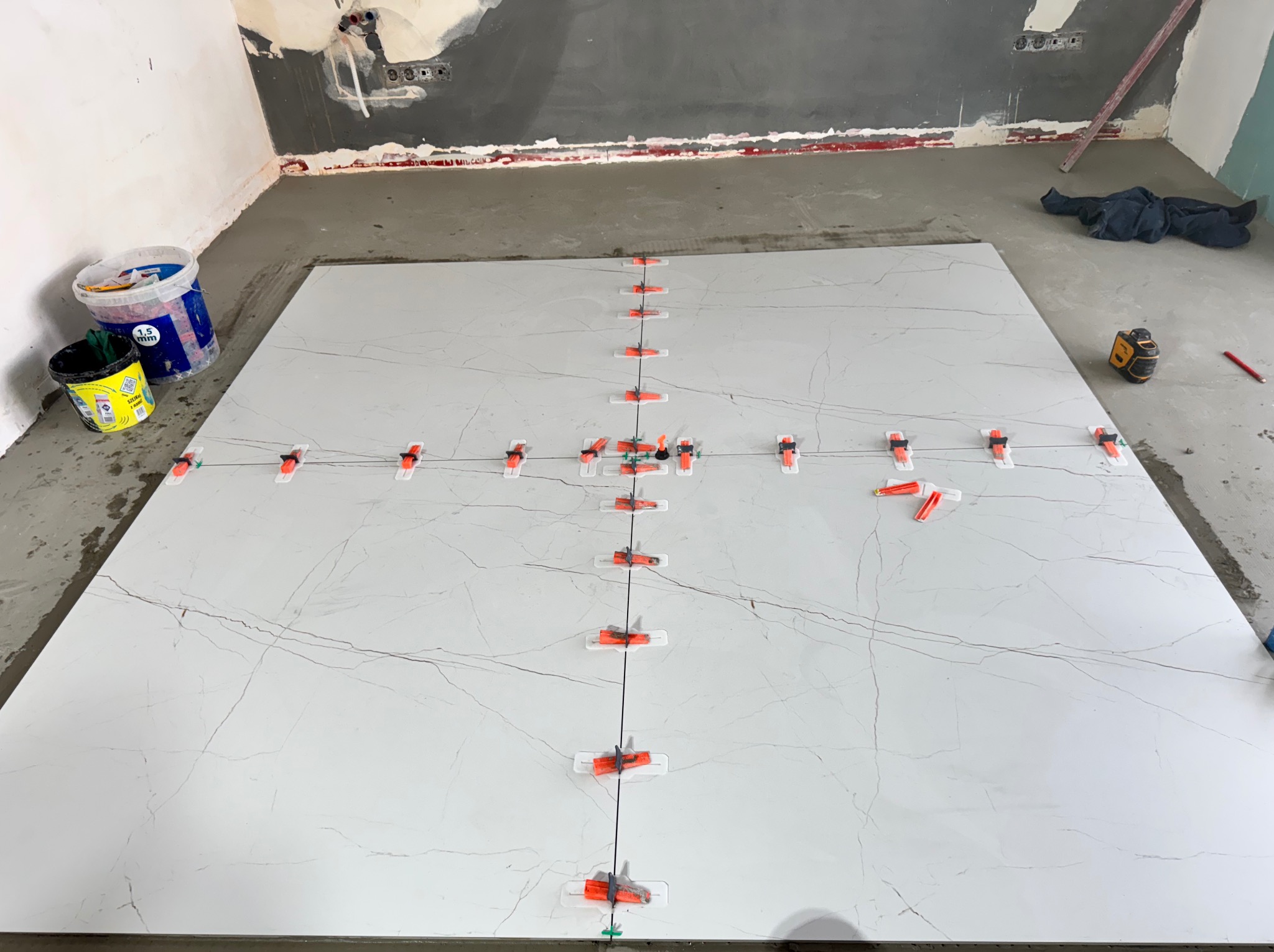 Układanie wielkoformatowych płytek podłogowych z użyciem systemu poziomowania. Widoczne krzyżyki dystansowe i poziomica laserowa. Przygotowanie do fugowania.