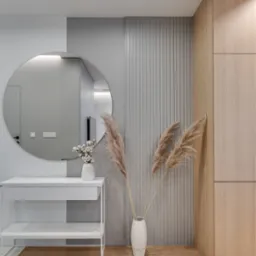 Nowoczesny przedpokój z okrągłym lustrem, białą konsolą, dekoracyjnymi trawami w wazonie i zabudową meblową z jasnego drewna.