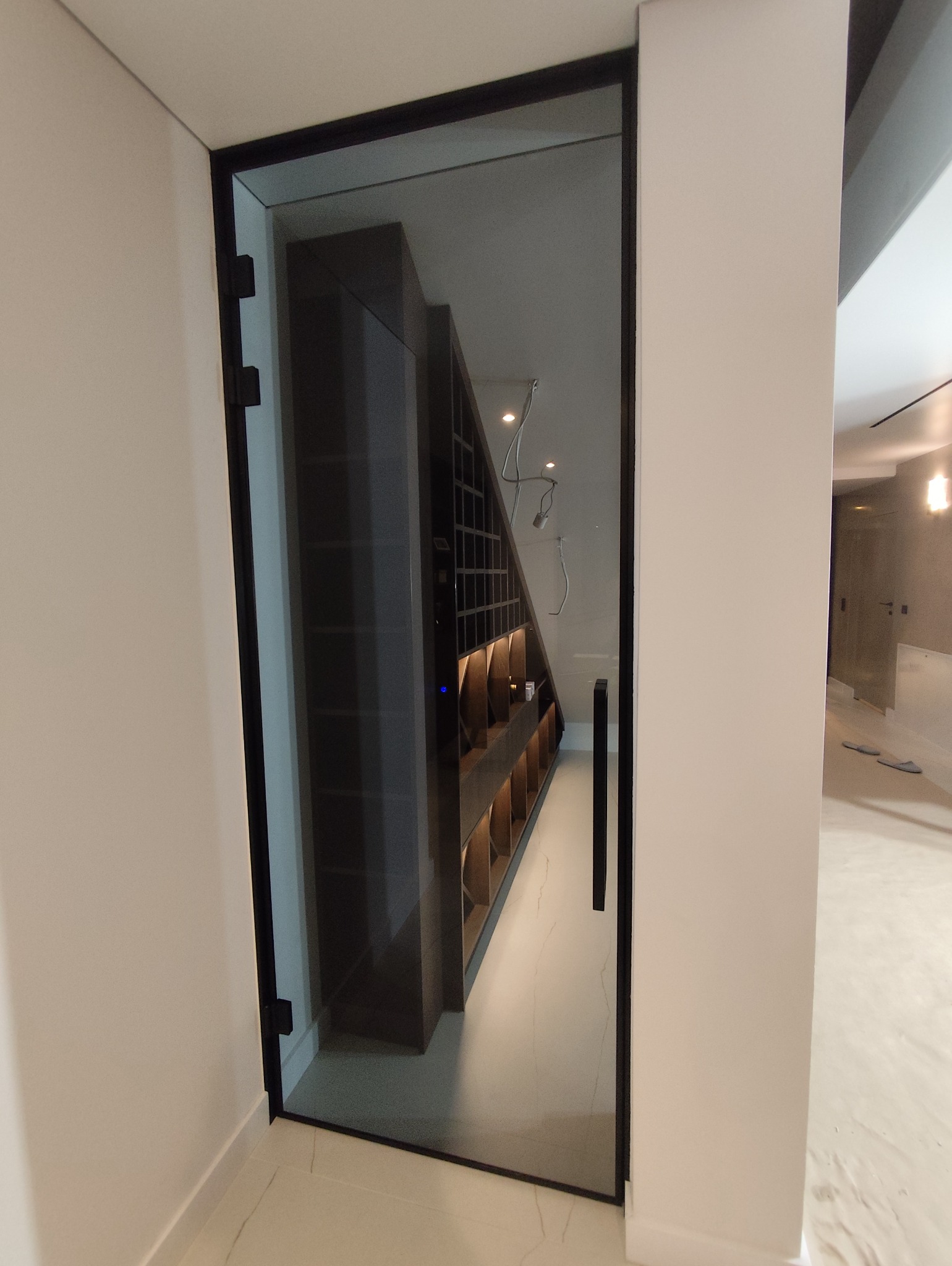 Szklane drzwi z czarną ramą prowadzące do pomieszczenia z regałem na wino, widok z boku.