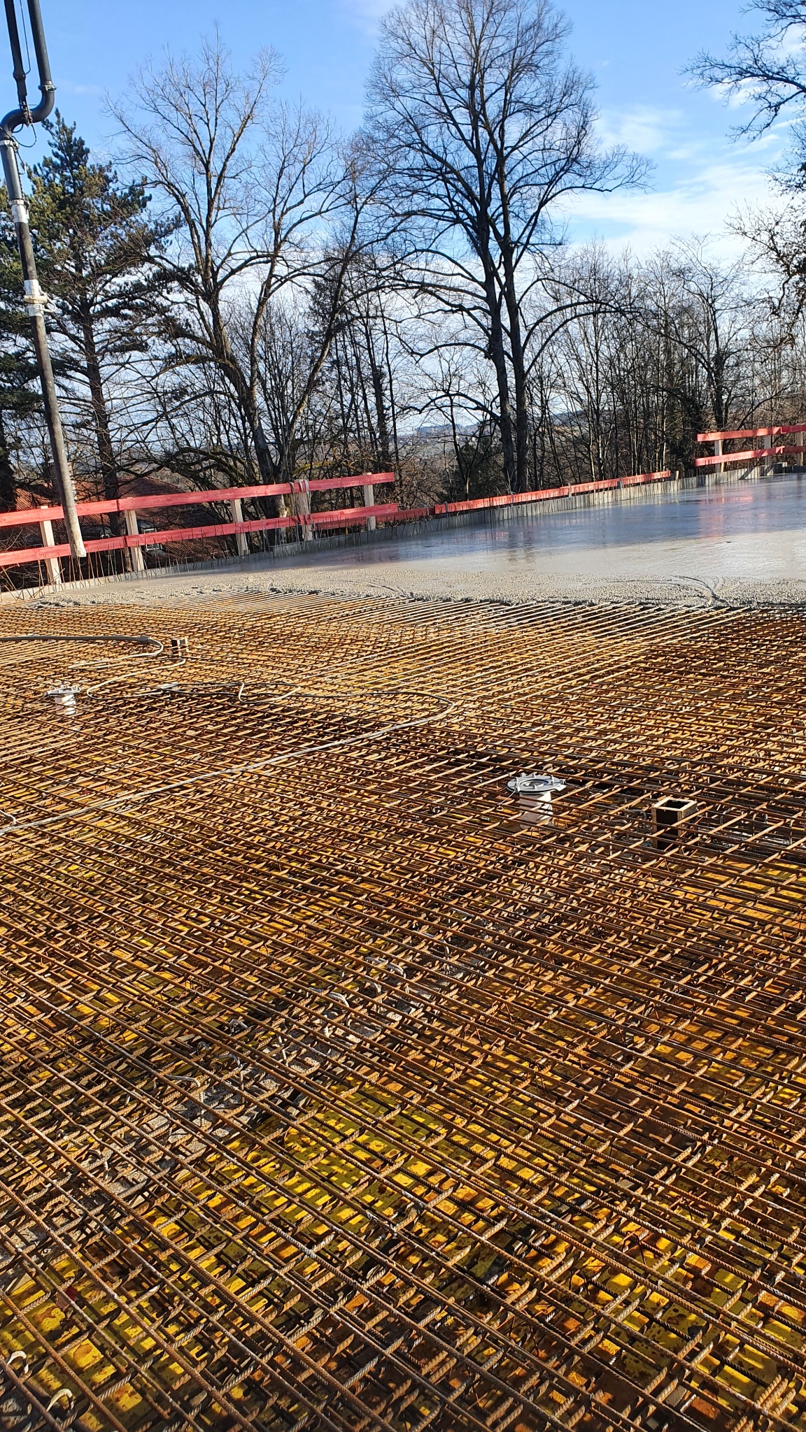 Zbrojenie ułożone na żółtej folii, częściowo zalane betonem na tle drzew i niebieskiego nieba.