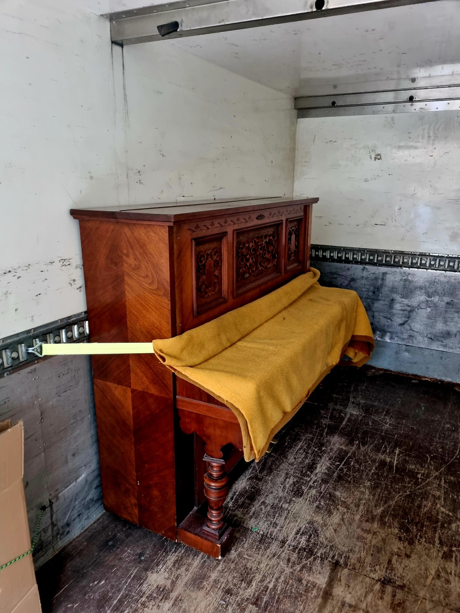 Pianino zabezpieczone pasem i kocem wewnątrz paki samochodu dostawczego podczas transportu.