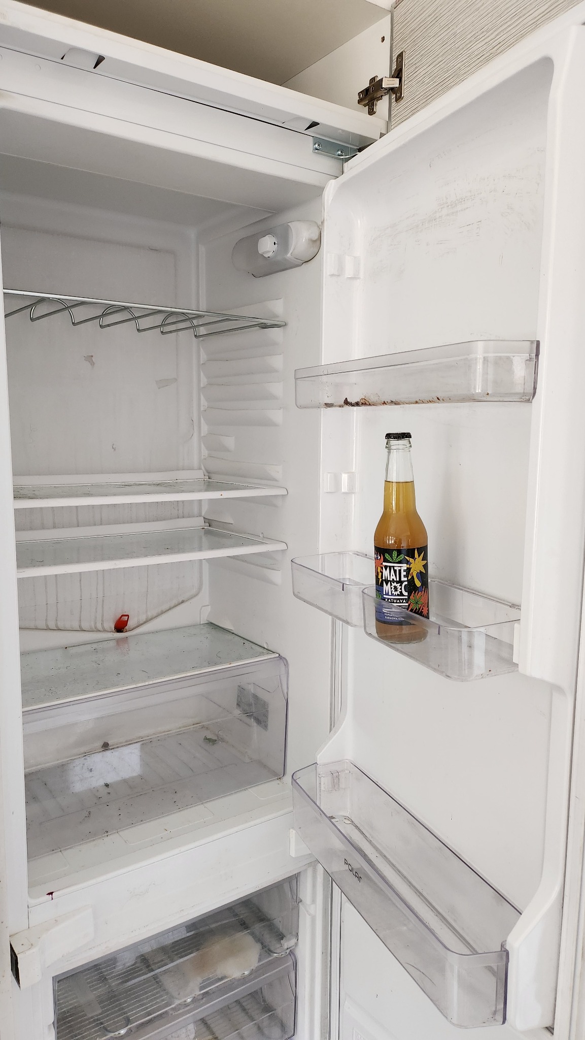 Wnętrze brudnej, białej lodówki marki Polar z jedną butelką napoju Mate Mec na półce w drzwiach.