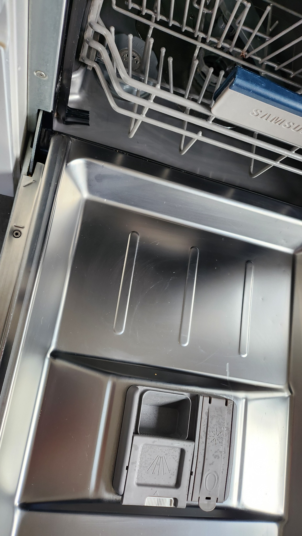 Wnętrze pustej, błyszczącej zmywarki Samsung, widok z góry na dolny kosz i dozownik detergentu z widocznymi śladami użytkowania.