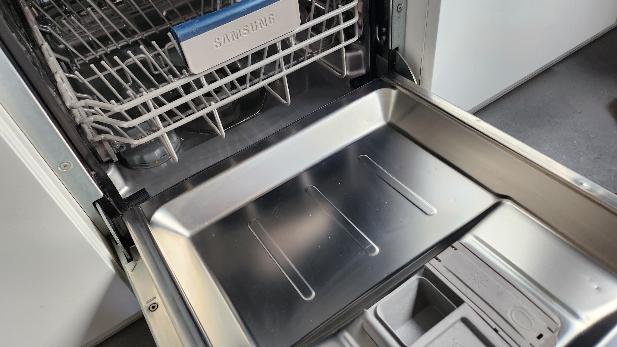 Wnętrze otwartej, pustej zmywarki marki Samsung, widoczne kosze i pojemnik na detergenty, gotowe do załadunku naczyń.