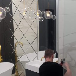 Radosław Radosław - Montaż szklanej kabiny prysznicowej w nowoczesnej łazience z lustrzaną ścianą w romby, złotą armaturą i wiszącymi lampami typu bubble.