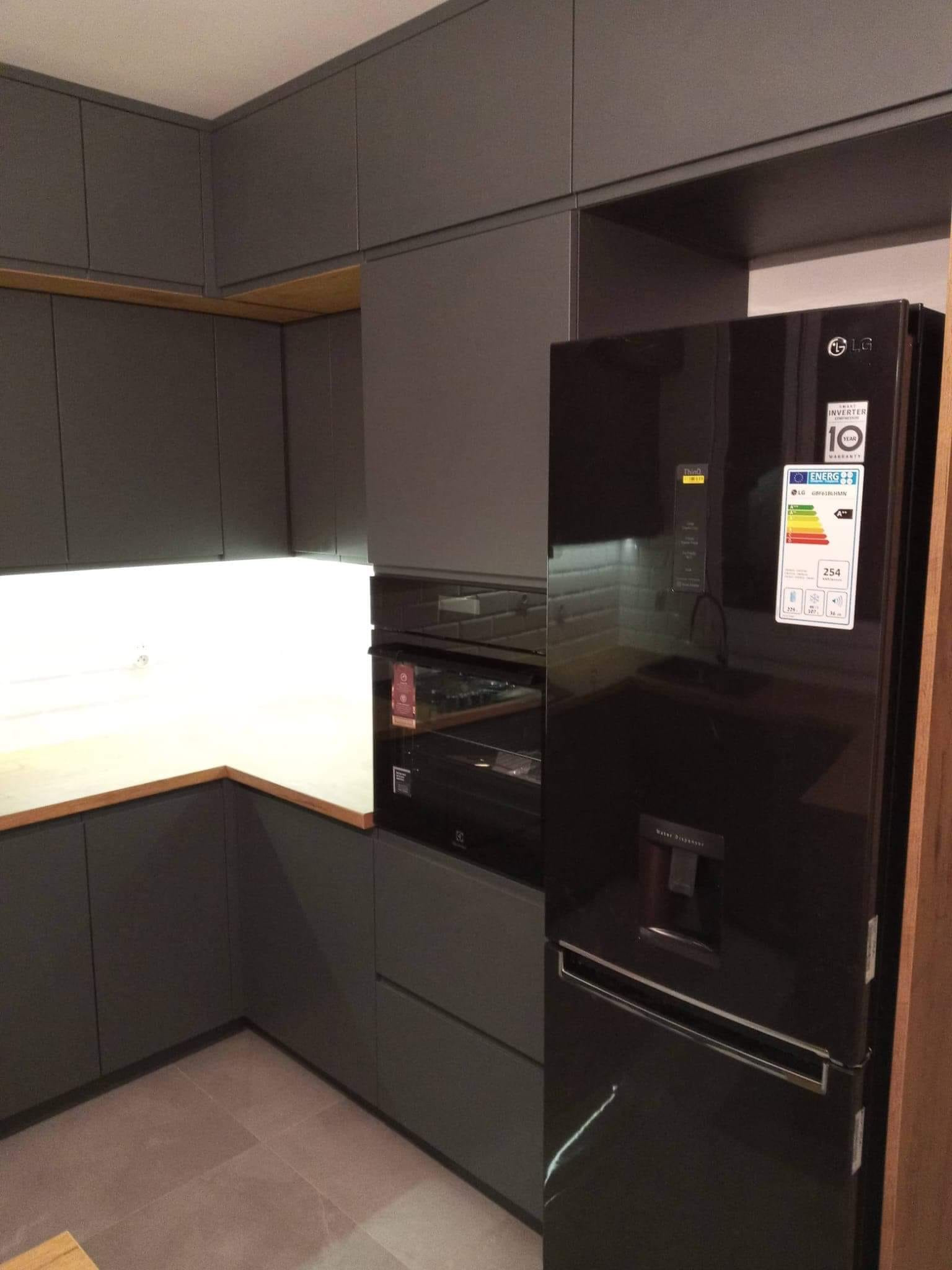 Nowoczesna kuchnia z szarymi szafkami, drewnianym blatem i czarną lodówką z dozownikiem wody.