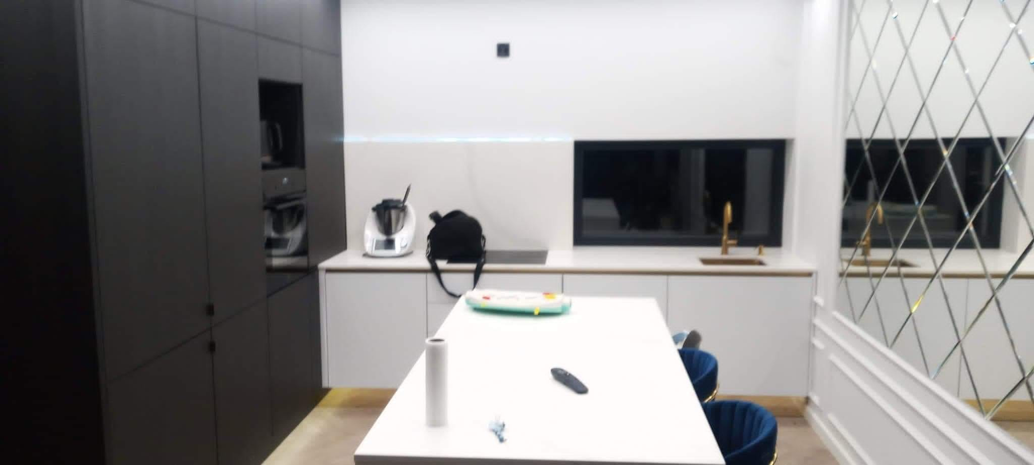 Nowoczesna kuchnia z ciemnymi szafkami, białą wyspą i lustrzaną ścianą z dekoracyjnymi listwami.