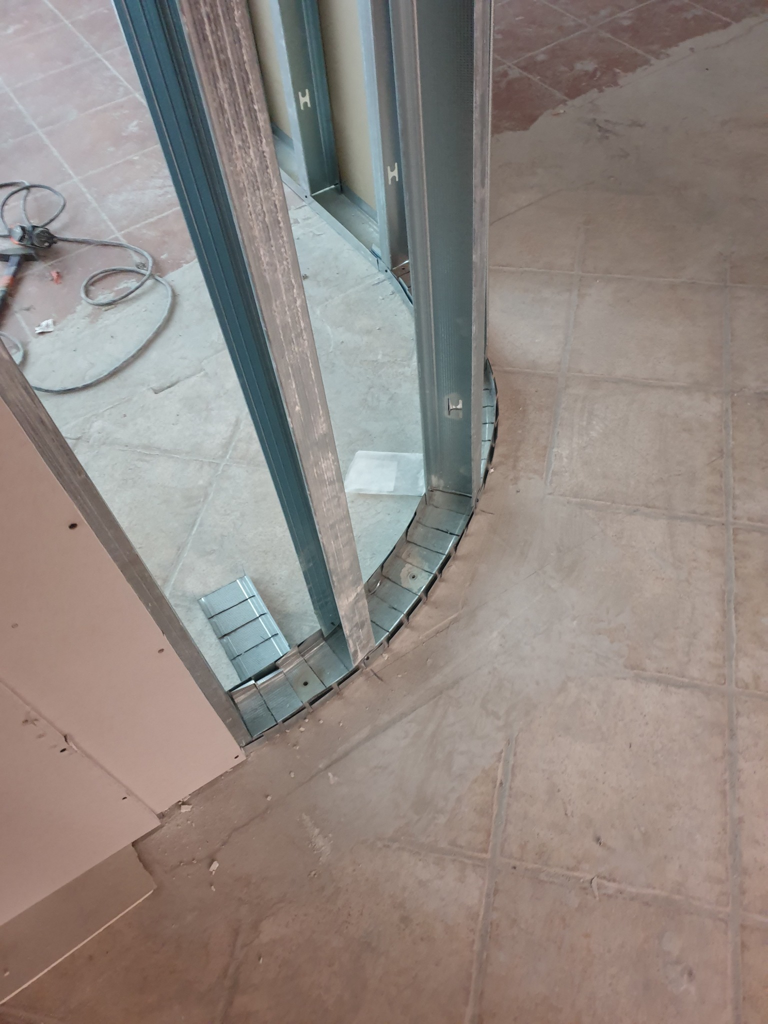 Konstrukcja z profili metalowych pod płytę karton gips, tworząca łukowate przejście w trakcie budowy ściany działowej, widok z góry na podłogę z płytek.