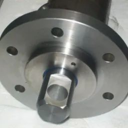 Metalowy element z kołnierzem i centralnym otworem o przekroju kwadratowym, widoczne ślady obróbki skrawaniem.