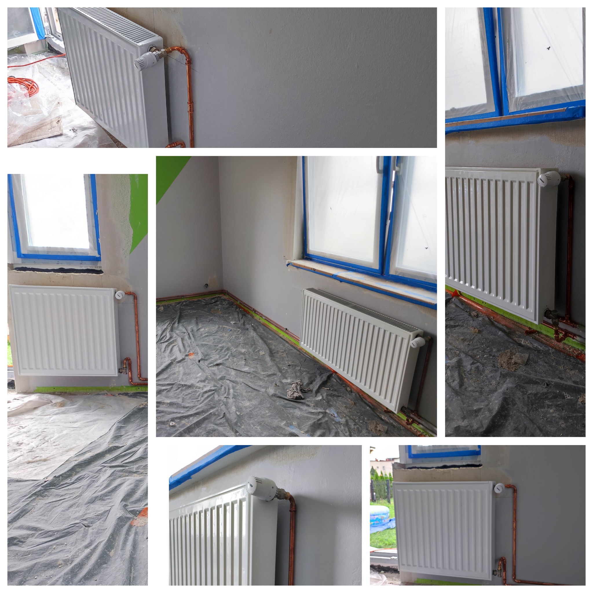 Biały grzejnik panelowy z miedzianymi rurami przy szarej ścianie, okno zabezpieczone folią malarską, podłoga przykryta czarną folią ochronną podczas prac wykończeniowych.