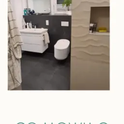 Nowoczesna łazienka z czarną ścianą, wiszącą toaletą i umywalką na szafce, dekoracyjna ściana z efektem falowania, roślina w oknie.