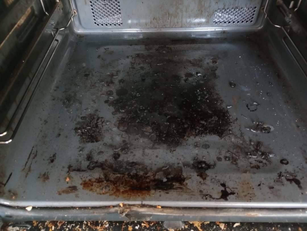 Brudna, przypalona blacha do pieczenia w piekarniku, widoczne resztki jedzenia i tłuszcz, metalowa konstrukcja piekarnika.